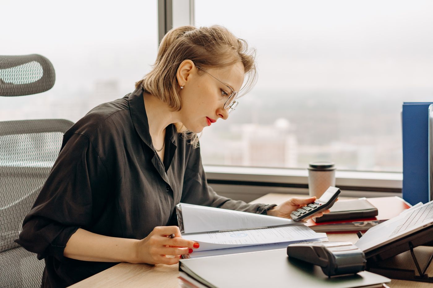 An accountant checking documents with a calculator at an office desk